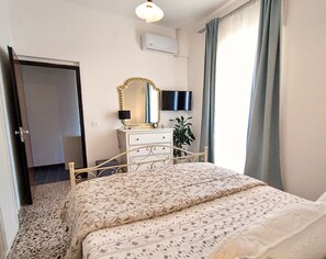 Un dormitorio con cama, cómoda, espejo, televisor y planta.