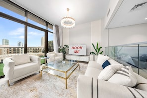 Ein modernes Wohnzimmer mit einem Glastisch, weißen Sofas, einer Kronleuchter und einem Schild mit der Aufschrift 'BOOK ME'.
