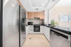 A modern kitchen with stainless steel appliances, wooden cabinets, and a black countertop. - Free Housekeeping Visits During Your Stay - Stayshort - Modern 3 Bedroom Duplex Apartment in JVC That Sleeps 5 (Dubai)