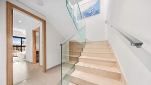 Ein modernes Interieur mit einer Treppe, Glasgeländern und Blick durch eine offene Tür.