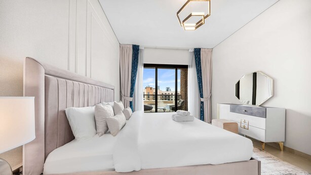 Ein Hotelzimmer mit einem großen Bett, einem Nachttisch, einer Kommode, einem Spiegel und Blick auf die Stadt.