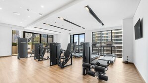A modern gym with exercise equipment, large windows, and a view of a cityscape. - Free Housekeeping Visits During Your Stay - Stayshort - Relaxing 1 Bed That Sleeps 4 With Amazing Views From Balcony (Dubai)