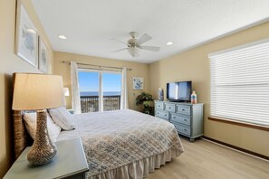 A bedroom with a bed, a TV, a dresser, a lamp, and a ceiling fan. - LISTEN TO THE SONG of the surf from this adorable island home. (St. George Island)