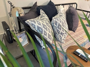Ein Bett mit gemusterten Kissen, eine Lampe, ein Bilderrahmen, eine Fernbedienung und ein kleiner Tisch mit einer Fernbedienung.