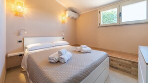 Une chambre à coucher comprenant un lit, deux lampes fixées au mur, un climatiseur, une fenêtre et un banc en bois.