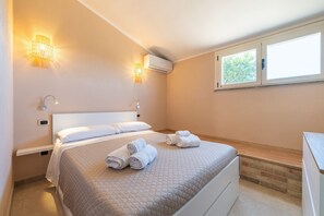 A bedroom with a bed, two wall-mounted lights, an air conditioner, a window, and a wooden bench. - Casa Adele Porto Luna (Simius)