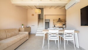 Un salon moderne comprenant un canapé, une table à manger et des chaises, un escalier menant à la cuisine et un appareil de climatisation.