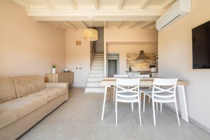 Ein modernes Wohnzimmer mit Sofa, Esstisch und Stühlen, einer Treppe zum Küchenbereich und einer Klimaanlage.