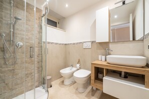 A bathroom with a glass-enclosed shower, a bidet, a toilet, and a wooden vanity with a sink. - Casa Adele Porto Luna (Simius)