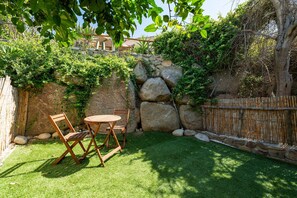 A patio with a table and chairs, surrounded by a stone wall and greenery. - Casa Adele Porto Luna (Simius)