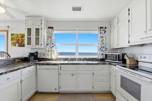 A kitchen with white cabinets, a dishwasher, a stove, a microwave, and a window with curtains. - BECOME AN ISLAND CASTAWAY in this cozy, fun in the sun, beachfront home. (St. George Island)