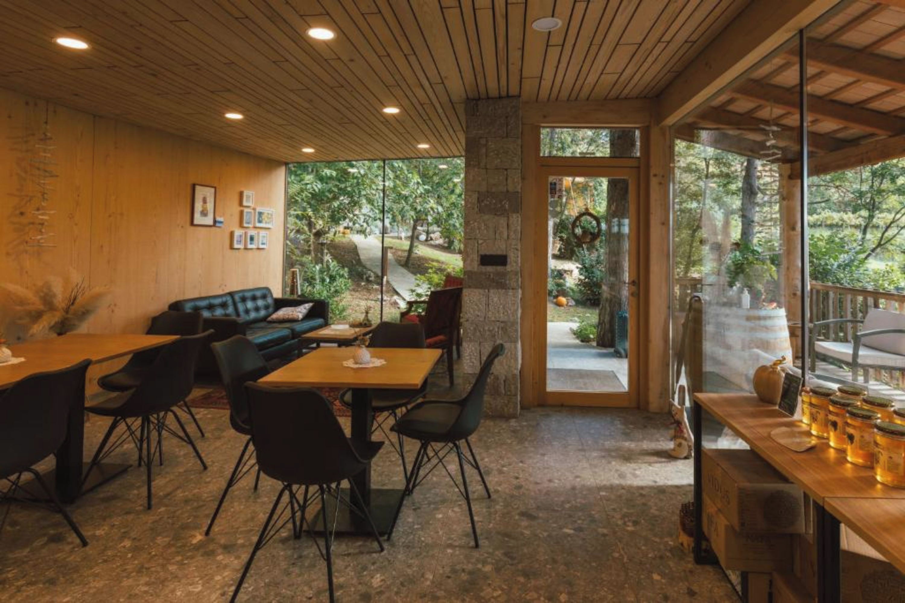 Un espace intérieur accueillant, avec un plafond en bois, un mur en pierre et une grande porte vitrée donnant sur un espace extérieur verdoyant.