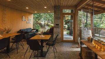 Un espace intérieur accueillant, avec un plafond en bois, un mur en pierre et une grande porte vitrée donnant sur un espace extérieur verdoyant.