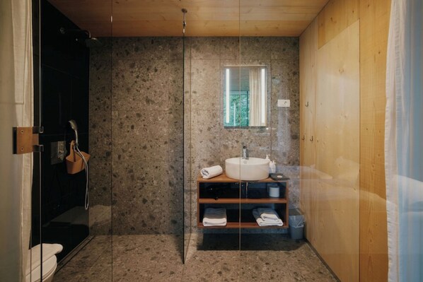 A bathroom with a glass shower enclosure, a wooden vanity with a sink, and a window providing natural light. - Theodosius Glamping Mobile Home (Vipava)