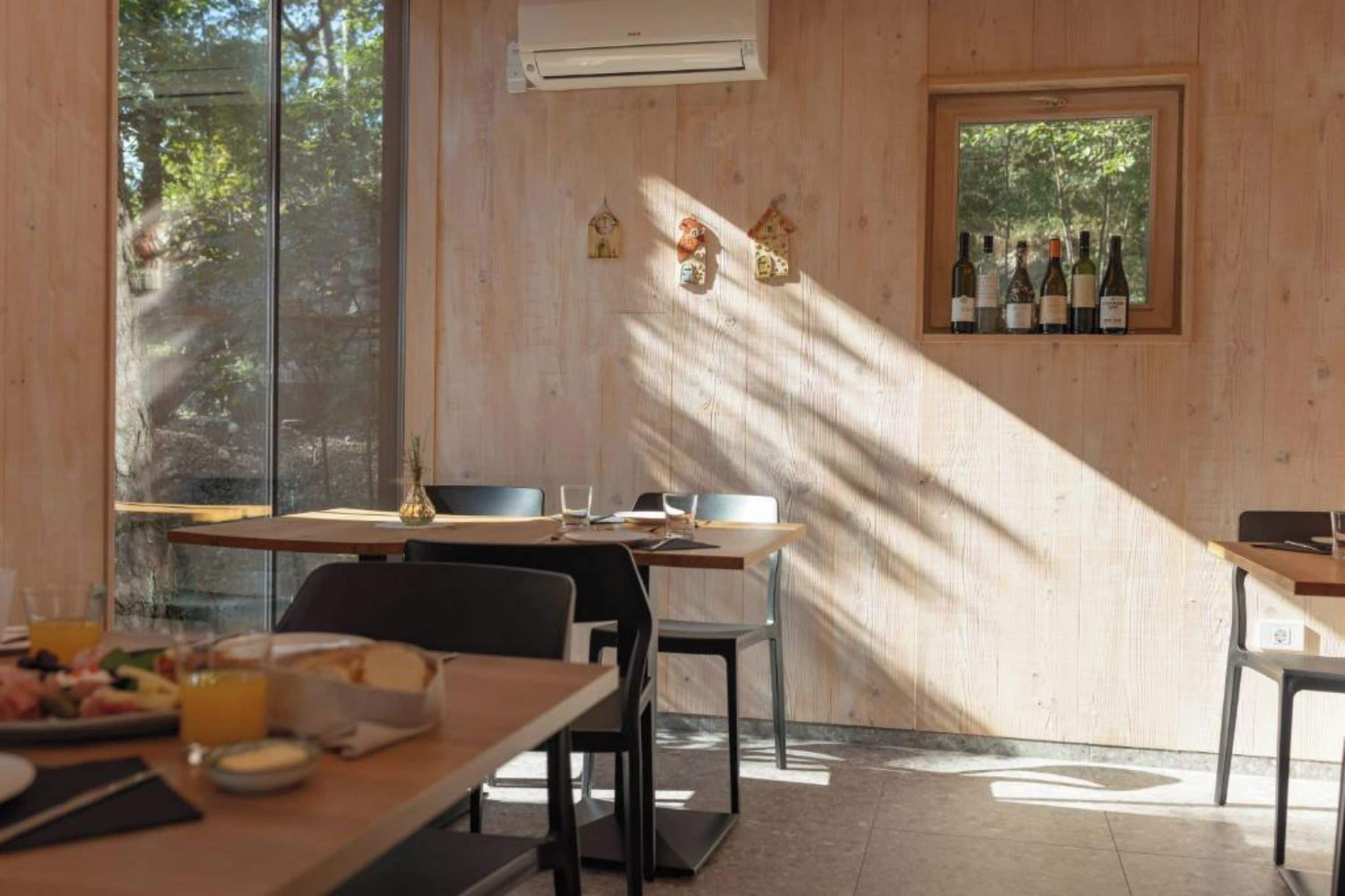 Uma sala de jantar com mesa de madeira, cadeiras e uma janela com garrafas.