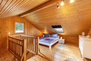 Ein Zimmer mit Holzboden und geneigter Decke, ausgestattet mit einem Bett mit Kissen, einem Nachttisch, einer Kommode und einem Fenster.