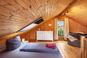 Una camera da letto mansardata accogliente con pareti in legno, un letto, un comò e un divano.
