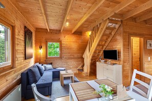 Ein Holzblockhaus-Innenraum mit einer Couch, einem Esstisch, einem Fernseher und einer Treppe.