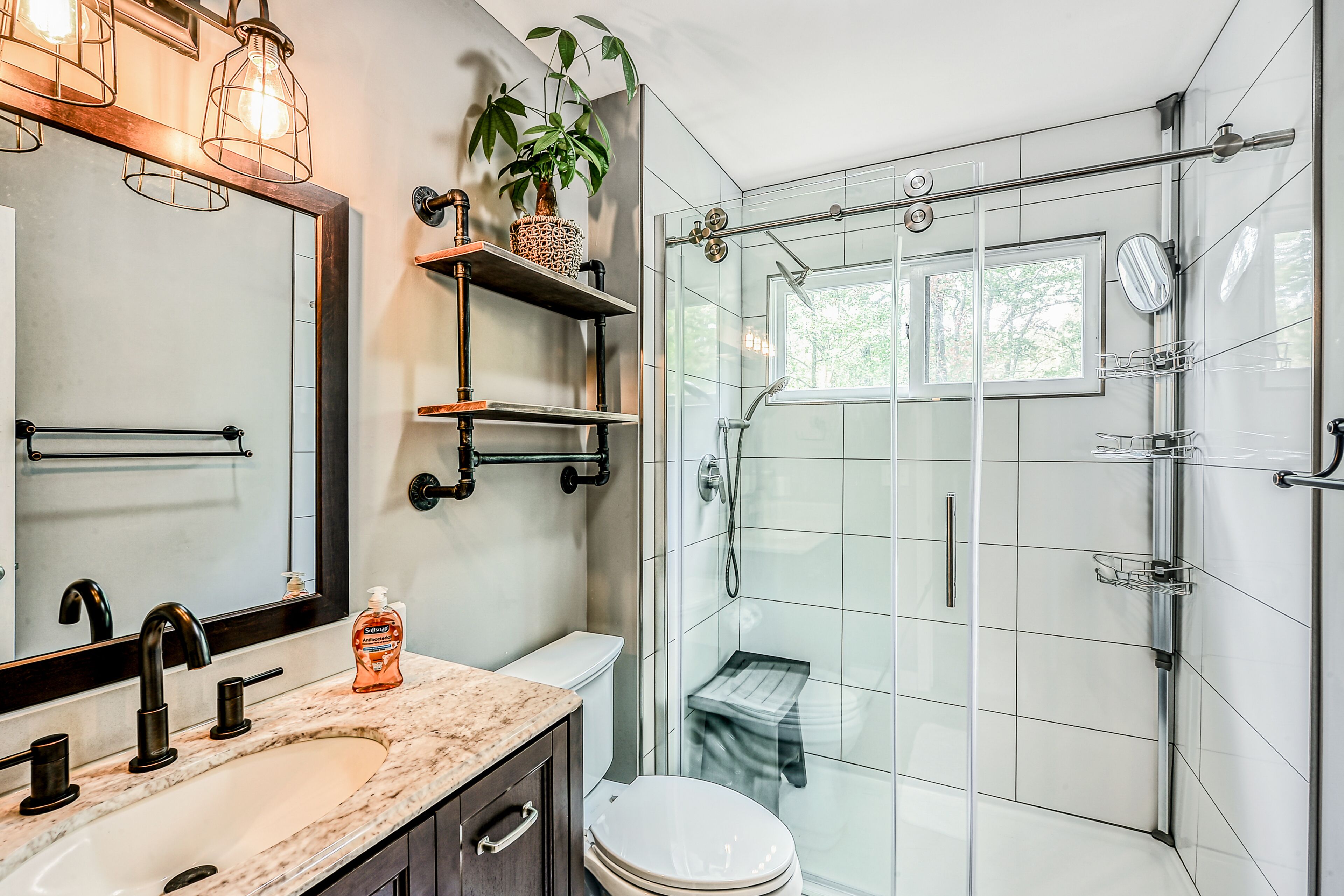 Een moderne badkamer met een marmeren wastafel, toilet, douche met glazen wanden en een spiegel met planken erboven.