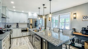 A modern kitchen with white cabinets, granite countertops, a central island, and pendant lighting. - Lakefront Home with Private Dock, Hot Tub, Fireplace, & Central A/C - Free WiFi (Bumpass)