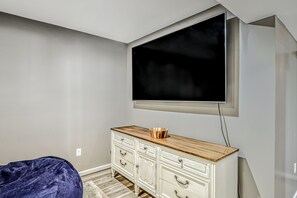 Habitació amb un cofre blanc, una televisió penjada a la paret i un seient de bossa blava.