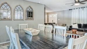 A dining area with a dark wooden table, white chairs, and a wooden bowl centerpiece. There are three arched windows on the wall. - Lakefront Home with Private Dock, Hot Tub, Fireplace, & Central A/C - Free WiFi (Bumpass)