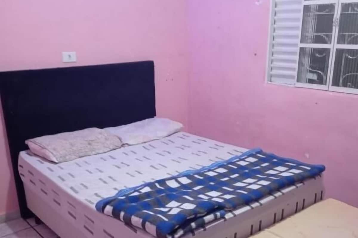 A single bed with a headboard, a window with blinds, and a tiled floor.