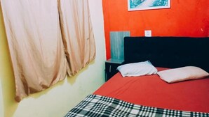 Un dormitorio con cama, cortinas, mesita de noche, lámpara y un cuadro colgado en la pared.