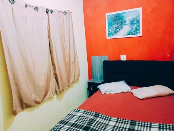 A bedroom with a bed, curtains, a nightstand, a lamp, and a wall-mounted picture. - Hostel Bryan Tatuape (São Paulo)