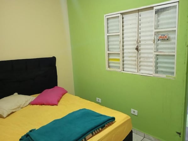A room with a bed, pillows, a window with blinds, and a wall with a sign. - Hostel Bryan Tatuape (São Paulo)