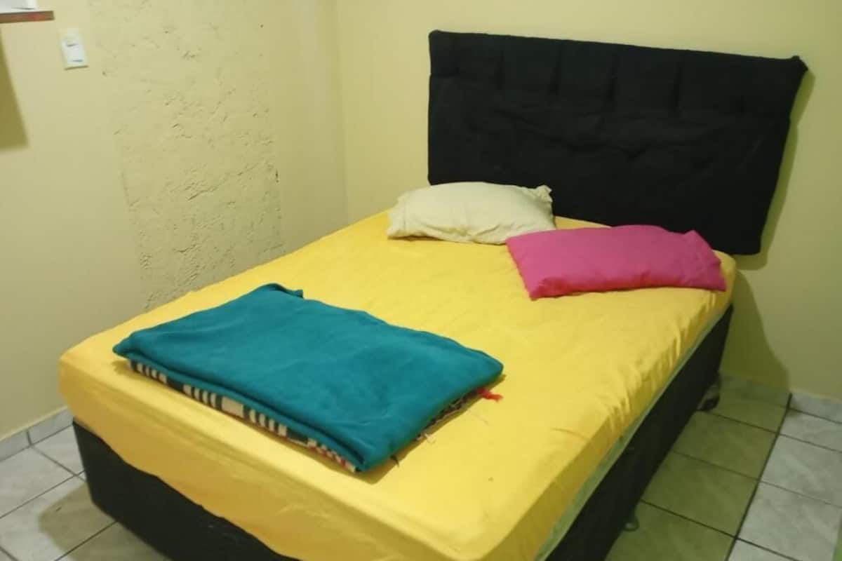 A single bed with a black headboard, yellow bedding, and two pillows.