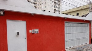 Un edificio rojo con una puerta de garaje blanca, una puerta blanca y una unidad de aire acondicionado, y un letrero con el número 69.