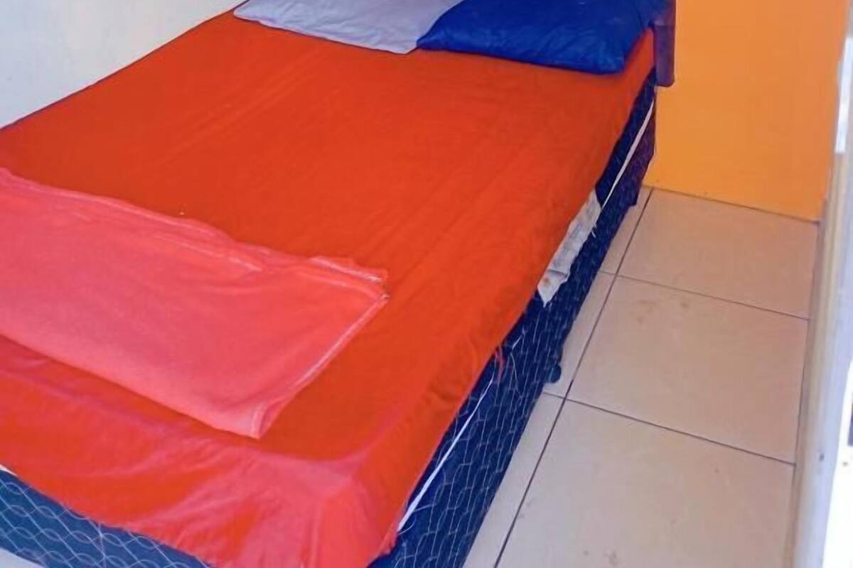 A single bed with an orange bedspread, a blue pillow, and a grey pillow. There are two framed pictures on the wall above the bed.