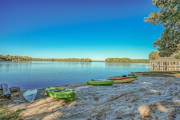 Um lago calmo com caiaques na margem, um gazebo e um céu azul e límpido.