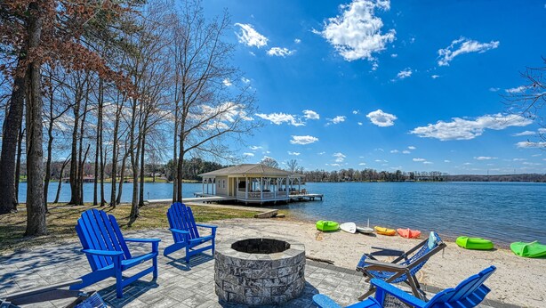 A lakeside deck with blue Adirondack chairs, a stone fire pit, and a wooden deck extending over the water. - 5BR and 5.5 BA Lakefront Home w/private hot tub and dogs ok! (Bumpass)
