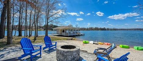 A lakeside deck with Adirondack chairs, a fire pit, and a gazebo by the water.