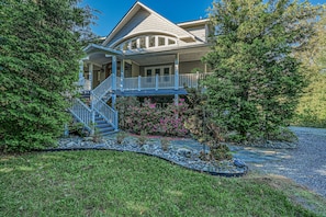 A two-story house with a covered porch, a staircase, and a well-maintained garden with various plants and a gravel driveway.