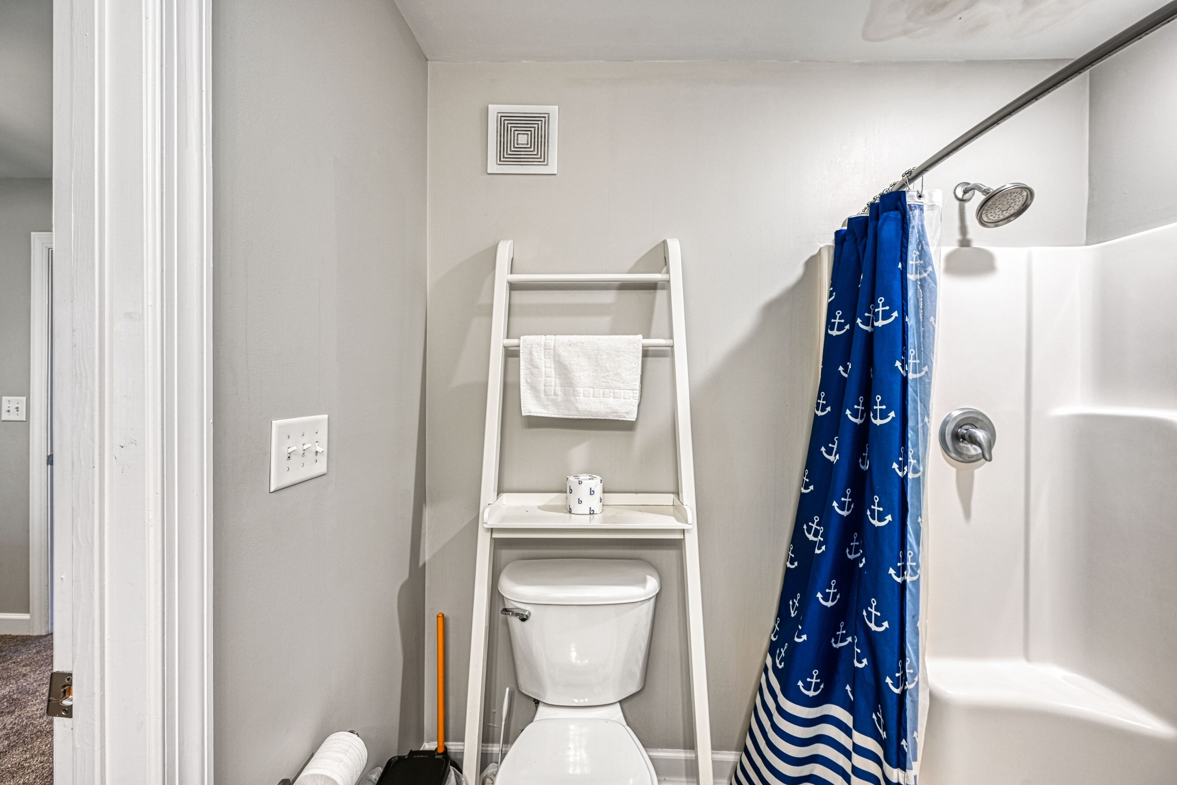 A bathroom with a white toilet, a white towel on a rack, a blue shower curtain with anchor patterns, and a white bathtub.