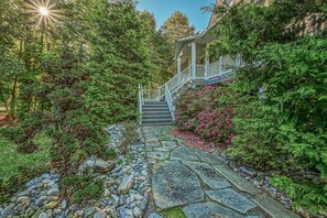 Un chemin de pierres menant à une maison dotée d’un porche et d’un escalier.