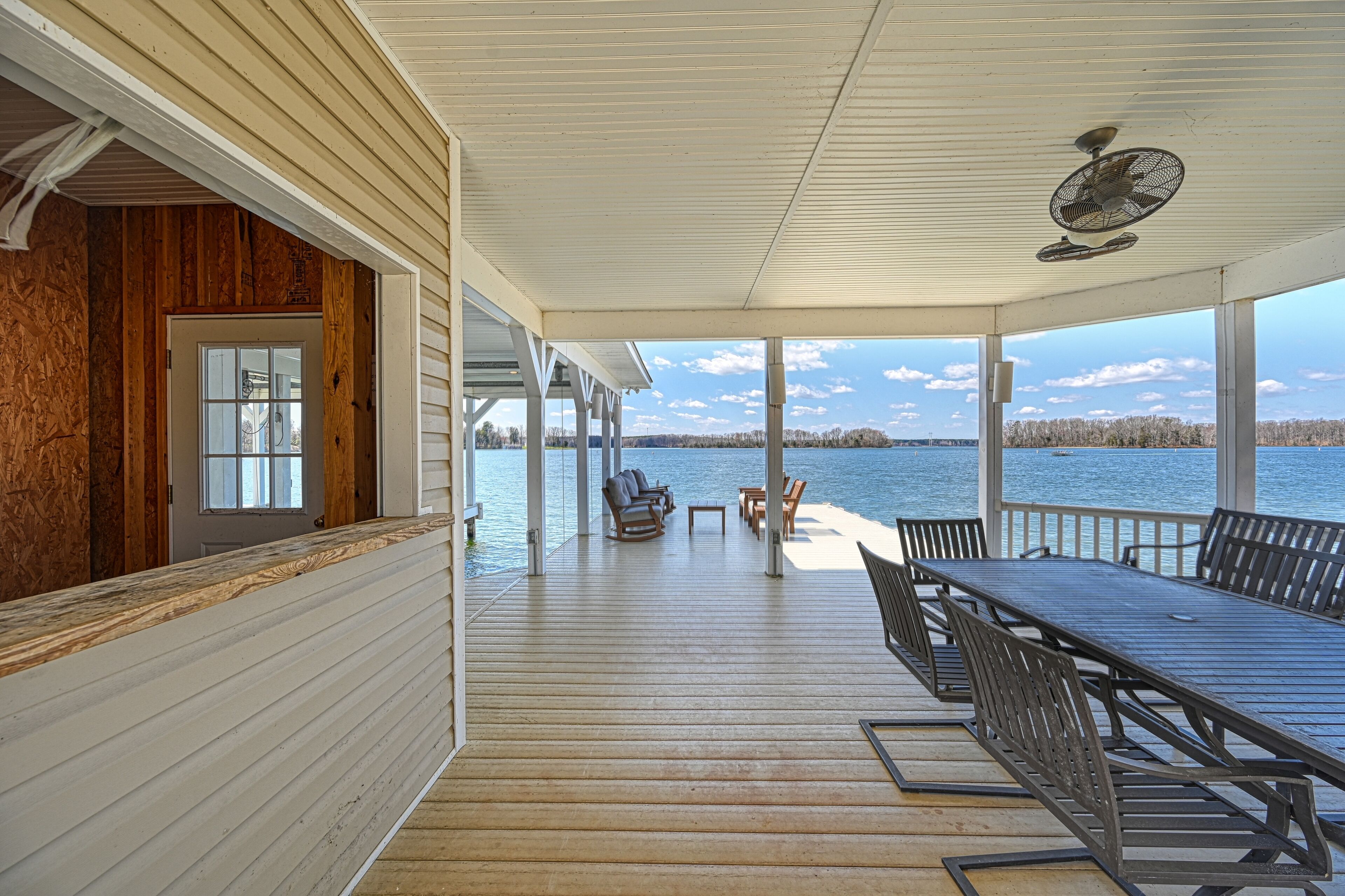 A covered deck with a table and chairs, overlooking a body of water.