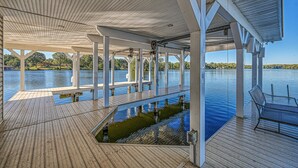 A covered deck with a view of a lake, wooden flooring, and a bench. - 5BR and 5.5 BA Lakefront Home w/private hot tub and dogs ok! (Bumpass)