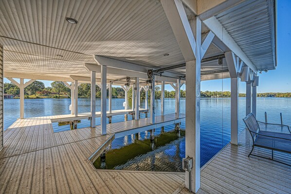 Una terraza techada con vista a un lago, piso de madera y un banco.