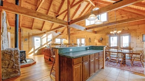 A spacious kitchen with wooden beams, a large island, and a dining area with a table and chairs. - Dog-friendly, lake view cabin w/ furnished decks, Ping-Pong & darts (Mineral)