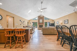 A spacious kitchen with wooden flooring, a central island with bar stools, and a dining area with chairs.