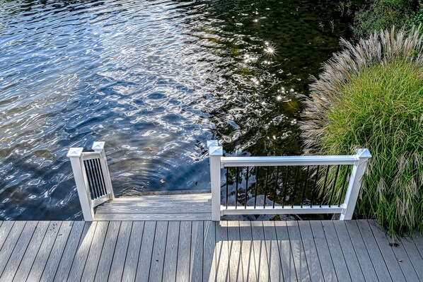 A wooden dock with a white railing leading to a body of water.