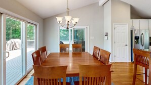 A dining area with a wooden table and chairs, a chandelier, and a view through glass doors to an outdoor deck.