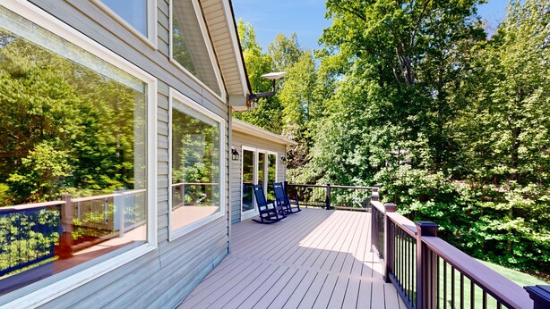 A deck with a railing, a pergola, and two chairs.