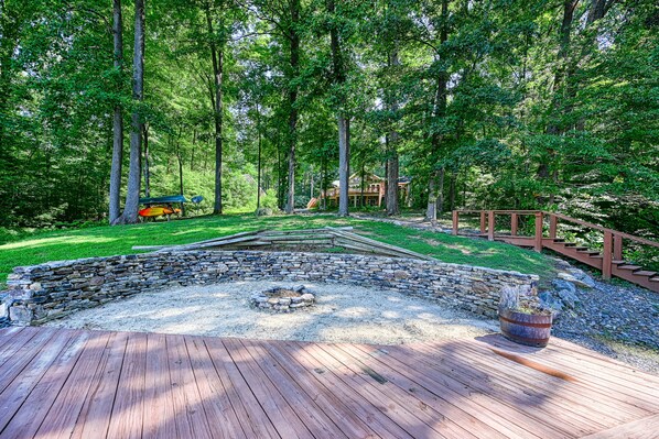 Una terraza de madera con un hogar de piedra y un espacio al aire libre rústico rodeado de árboles.