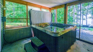 Un jacuzzi en un área exterior cubierta con amplios ventanales, vigas de madera y vista a un bosque.