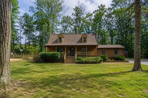 A two-story wooden house with a front porch, a small attached garage, and a well-maintained lawn. - Lake Anna home on large corner lot with kayaks, paddleboard, firepit & grill (Bumpass)